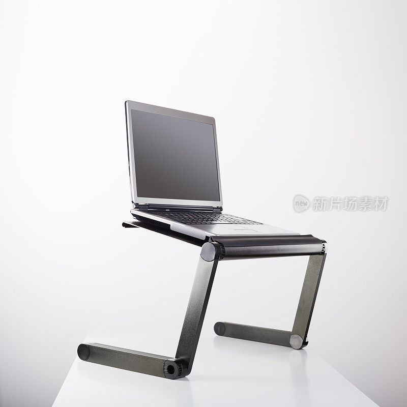 Laptop computer sits on a portable holder riser or stand against white background